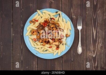 Vegetarische gesunde Lebensmittel. Waldpilze goldene Pfifferlinge und Pasta Penne mit Chili-Pfeffer in blauer Platte auf dunklen rustikalen Hintergrund copyspace abov Stockfoto