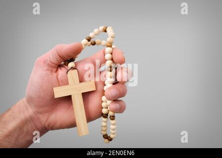 Christliches Holzkreuz mit runden Holzperlen auf der Hand Von einem Gläubigen mit isoliertem grauen Hintergrund Stockfoto