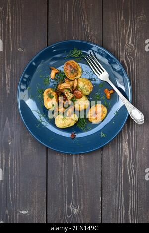 Vegane skandinavische Mahlzeit. Gebratene Kartoffeln, Waldpilze Pfifferlinge und Dill auf marineblauer Platte auf rustikalem dunklem Holz Hintergrund oben Ansicht Copyspace Stockfoto