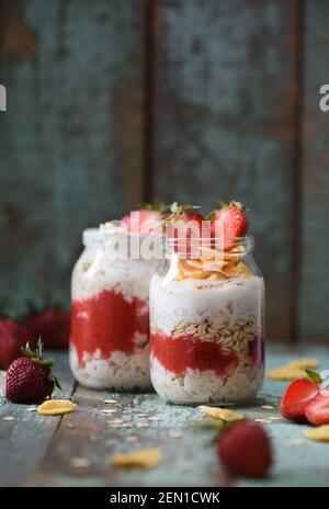 Gesundes nahrhaftes glutenfreies Frühstück. Über Nacht Hafer mit Bio-Erdbeere und Cornflakes in Gläsern auf schäbigen blauen Hintergrund Copyspace vert Stockfoto