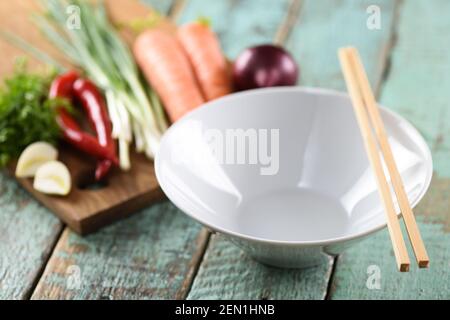 Leere weiße Schüssel und rohes Gemüse, Zutaten für asiatische udon-Nudeln mit Stöcken auf Holz blauen Hintergrund Nahaufnahme Stockfoto