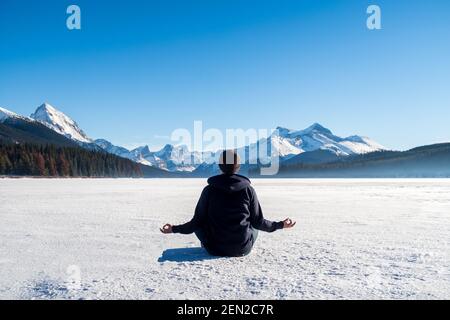 Junger Mann meditiert auf dem gefrorenen Maligne Lake im Jasper National Park, Kanada Stockfoto