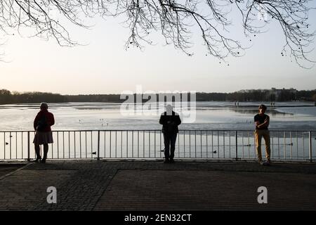 Berlin, Deutschland. Februar 2021, 25th. Drei Besucher genießen Sonnenschein am Tegeler See, bedeckt mit dünnem Eis in Berlin, Hauptstadt Deutschlands, 25. Februar 2021. Quelle: Shan Yuqi/Xinhua/Alamy Live News Stockfoto