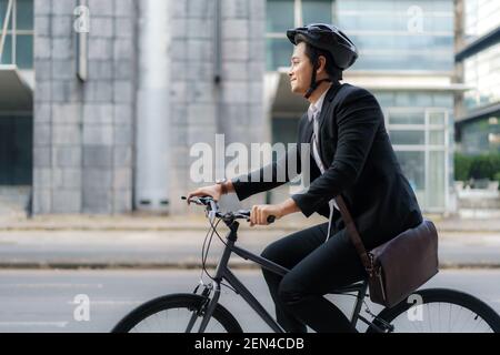 Asiatischer Geschäftsmann in einem Anzug fährt mit dem Fahrrad auf den Straßen der Stadt für seinen Morgen pendeln zur Arbeit. Eco Transportkonzept. Stockfoto
