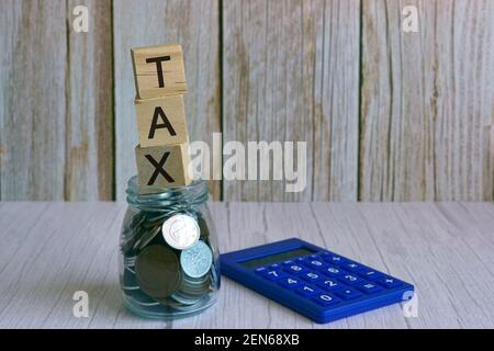 Steuertext auf Holzblock-Würfel auf Glasgefäß mit Mehrkurrency-Münzen Stockfoto