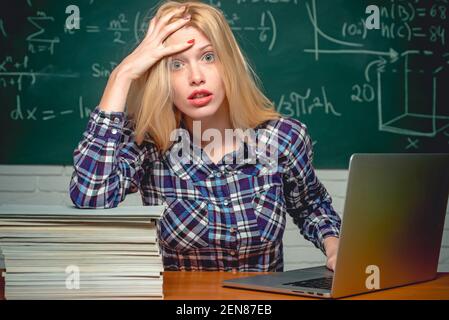 Verzweifelte Frau Student auf Klassenzimmer Hintergrund. Junge Lehrerin, die am Tisch sitzt und auf dem Notizbuch schreibt. Stockfoto