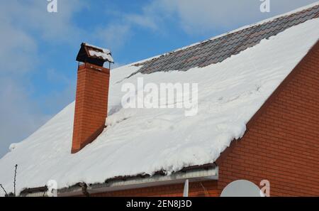 Ein steiler Hang Metalldach mit Schnee bedeckt mit einem Kamin, Regenrinnen, aber ohne Schneeschutz im Winter. Schnee gleitet, fällt von einem Metalldach. Stockfoto