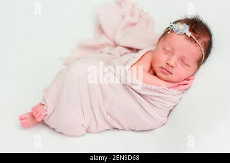 Nettes neugeborenes Baby Mädchen mit einem Verband auf ihrem Kopf Schläft mit gefalteten Händen unter ihrer Wange Stockfoto