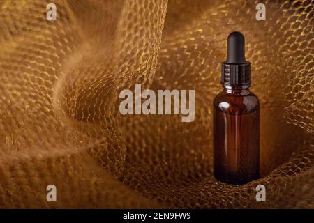 Kosmetische Glasflasche mit Pipette Tropferspender auf Hintergrund von goldenem Honig Mesh mit weichem Fokus. Studioaufnahme mit Kopierbereich. Pflege der Gesichtshaut Stockfoto