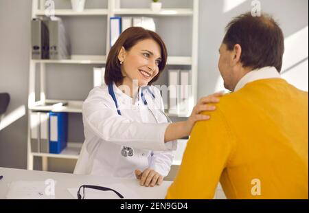 Lächelnder Arzt berührt die Schulter des älteren Mannes, unterstützt ihn und begrüßt ihn Er in der Klinik Stockfoto