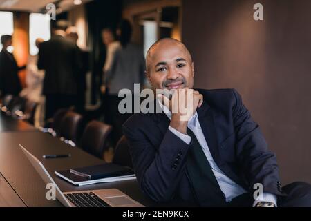Portrait von lächelnd kahlen männlichen professionellen sitzen mit der Hand auf Kinn am Konferenztisch im Konferenzraum Stockfoto