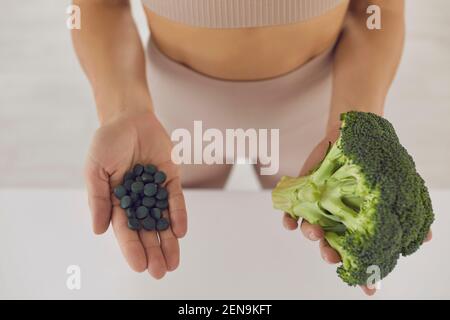 Nahaufnahme der Hände der Frau mit einem Kopf aus frischem Brokkoli Und Spirulina Tabletten Stockfoto