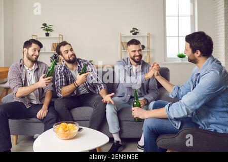 Gruppe von Freunden sitzen auf der Couch, trinken Bier und machen Spaß Wetten miteinander Stockfoto
