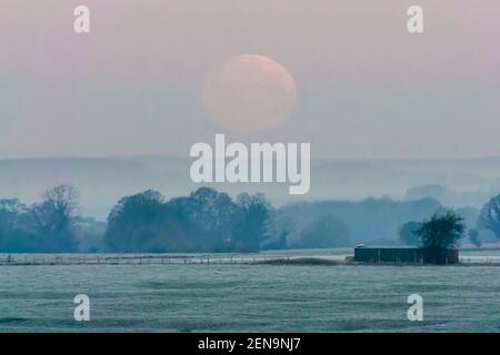 Amesbury, Wiltshire, Großbritannien. 26th. Februar 2021. Wetter in Großbritannien. Der fast Vollschneemond untergeht in der Nähe von Amesbury in Wiltshire kurz vor Sonnenaufgang an einem kalten frostigen Morgen. Bild: Graham Hunt/Alamy Live News Stockfoto