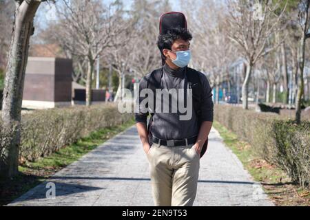 Latein junger Mann trägt eine schützende Gesichtsmaske, die eine Gitarre in einem Gitarrenkoffer auf einer Stadtstraße trägt. Universitätsgelände. Stockfoto