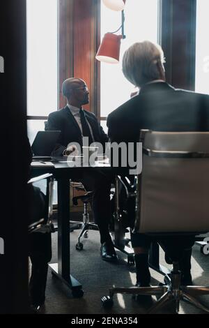 Männliche Profis blicken weg, während sie an einem Konferenztisch sitzen Sitzungssaal während der Besprechung Stockfoto