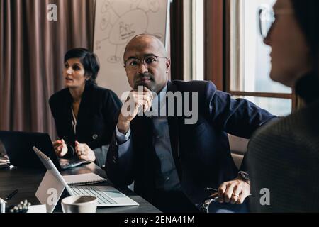 Porträt des selbstbewussten kahlen Geschäftsmann sitzt mit Hand auf Kinn Inmitten weiblicher Kollegen im Vorstandszimmer während des Meetings Stockfoto