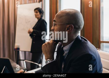 Bald Geschäftsmann mit Hand auf Kinn mit weiblichen Kollegen in Sitzungssaal während der Besprechung Stockfoto