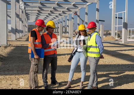 Gruppe von Geschäftsleuten in Hardhats diskutieren ein Projekt auf der Baustelle. Projektmanagement und Feldbesatzung auf Baustelle. Stockfoto