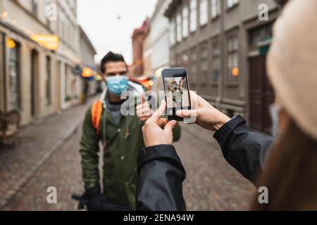 Zugeschnittenes Bild einer Frau, die während des Fotografierens einen Mann über ein Smartphone fotografiert Pandemie Stockfoto