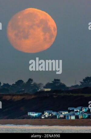 New Forest, Hampshire. 26th. Februar 2021. Wetter in Großbritannien. Der Mond geht über Strandhütten in Milford on Sea im New Forest unter. Der Vollmond im Februar, der als Schneemon bekannt ist, wird morgen um 8,18am Uhr in vollen Zügen erscheinen. An diesem Wochenende wird es kaum Schnee geben, mit einem hellen und sonnigen Wetter für die Südküste. Credit Stuart Martin/Alamy Live News Stockfoto