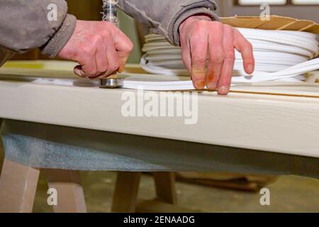 Ein Zimmermann verwendet improvisiertes Handwerkzeug und legt einen Gummi zum Abdichten auf den hölzernen Türrahmen. Stockfoto