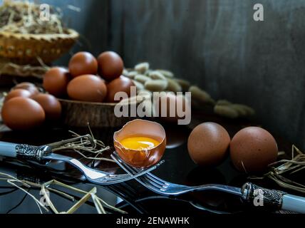 Gebrochenes frisches Hühnereier (Hühnereier) ausgewogen auf einer Komposition aus zwei miteinander verflochtenen Gabeln mit frischen Hühnereiern auf Holzhintergrund. Selektiver Fokus. Stockfoto