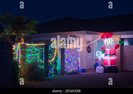 Weihnachtsdekoration auf einem Vorstadthaus in der Nacht. Bunte Lichter und ein aufblasbarer Weihnachtsmann Stockfoto