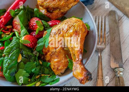 Kohlenhydratarme Mahlzeit mit gebratenem Huhn und süßem Chili-Spinat Erdbeersalat mit Kürbiskernöl auf einem Teller serviert Mit rustikalem Messer und Gabel Stockfoto