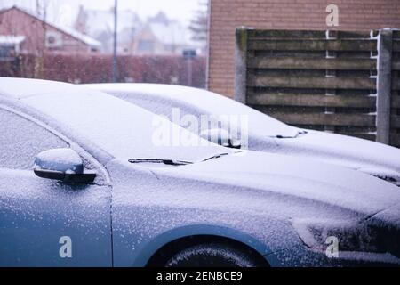 Ein Seitenportrait von zwei Autos während eines Schneesturms. Beide Fahrzeuge bekommen viel Schnee auf sie, so dass sie komplett weiß. Der Schnee sollte Onkel bekommen Stockfoto