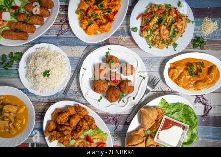 Auswahl an indischen Speisen einschließlich Curry, Reis, Samosas auf Holzhintergrund Stockfoto