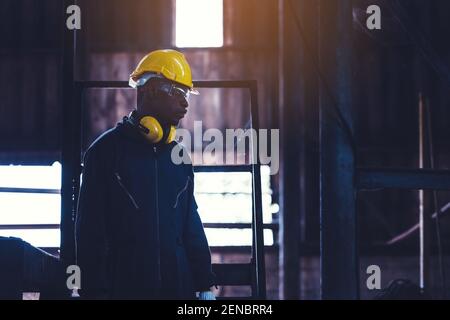 Portrait Arbeiter Mann mit gelbem Helm und Ohrenschutz in der Fabrik, Dunkler Ton Stockfoto
