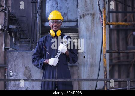 Portrait Arbeiter Mann mit gelbem Helm und Ohrenschutz in der Fabrik, Dunkler Ton Stockfoto
