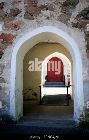 Eingang einer mittelalterlichen Steinkirche mit sonnenbeschienenen hölzernen Haupttür auf dem Hintergrund. Stockfoto