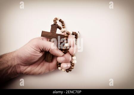 Hand eines kaukasischen religiösen Mannes, der sich fest vor Schuld ergreift Reue ein dunkelbraunes Kreuz mit runder Halskette aus Holzperlen Mit isoliertem Bac beten Stockfoto