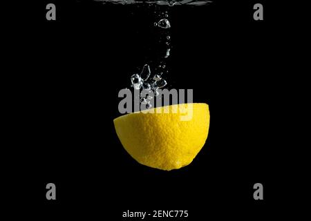 Frische gelbe Zitrone im Wasser Spritzer isoliert auf schwarzem Hintergrund. Minimales Lebensmittelkonzept.