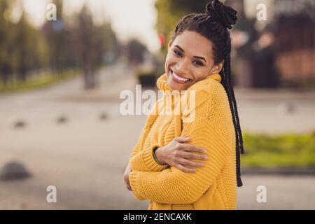 Foto von jungen glücklich positive fröhlich charmant afro Frau umarmen Selbst tragen gelben Pullover draußen im Freien Stockfoto