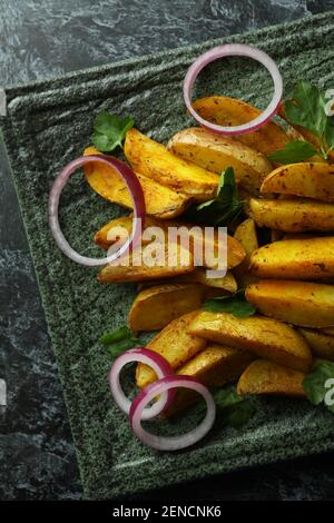 Teller mit Kartoffelkeilen, Petersilie und Zwiebel auf schwarzem rauchigen Hintergrund Stockfoto