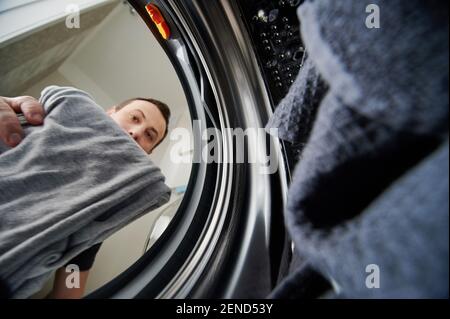 Mann, der schmutziges Tuch in die Waschmaschine einlädt, Blick von innen Stockfoto