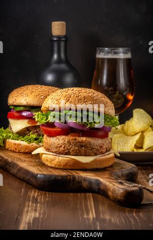 Zwei frische leckere Burger mit einem Glas Bier auf einem rustikalen Holztisch. Hintergrund für das Essen. Stockfoto