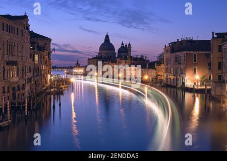 Venedig bei Nacht. Stadtbild des Canale Grande in Venedig, mit der Basilika Santa Maria della Salute im ruhigen Meer. Die Lichter des Passagierschiffs sind eingeschaltet Stockfoto