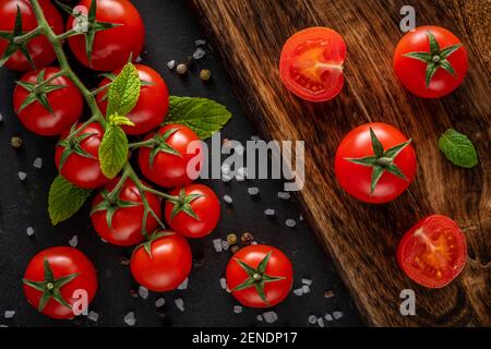 Frische Kirschtomaten auf schwarzem Hintergrund mit Gewürzen. Hintergrund für das Essen. Draufsicht. Stockfoto