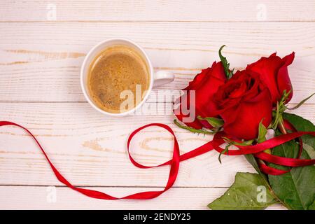 Tasse Kaffee und rote Rosen auf weißem Holzhintergrund. Valentinstag romantisches Frühstück Wohnung Lay Top View Frühstück Konzept. Stockfoto