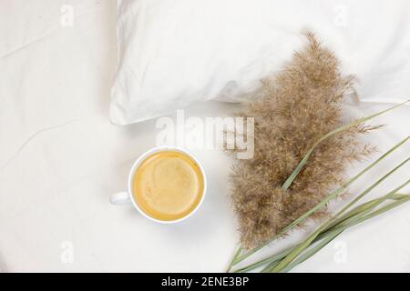 Tasse Kaffee und Pampagras auf weißem Bett. Morning romantisches Konzept. Flat Lay, Draufsicht, Bild. Stockfoto