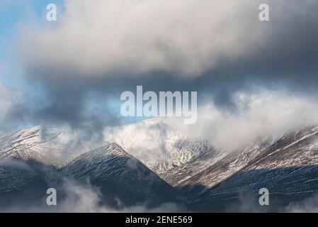 Atemberaubende Landschaft Bild von Skiddaw schneebedeckten Bergkette in Lake District im Winter mit niedrigen Wolken um Gipfel Stockfoto