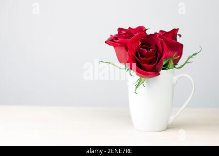 Roter Rosenstrauß in weißer Tasse auf Holzhintergrund. Valentinstagsgutschein mit Kopierplatz. Stockfoto