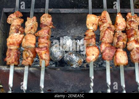 Gebackene Kartoffeln in Folie, auf Holzkohle im Grill, in der Natur, mit Schweinefleisch Kebab auf der Oberseite Stockfoto