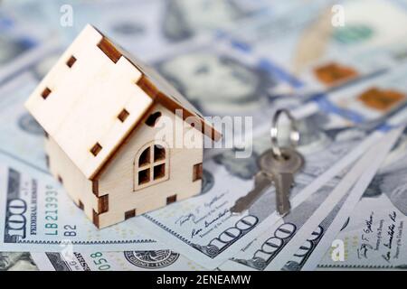 Holzhausmodell und Schlüssel auf dem Hintergrund von US-Dollar-Banknoten. Wohnungsmarkt, Kauf oder Vermietung von Immobilien Stockfoto
