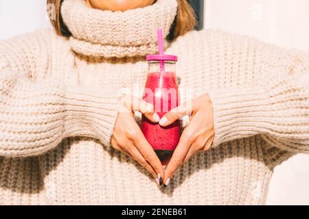 Frau macht Herzform mit ihren Händen und Flasche mit Smoothie. Gesundes Herz Stockfoto