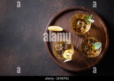 Drei Gläser Whiskey serviert auf Felsen mit Zitrone für festliche Party auf braunem Hintergrund. Speicherplatz kopieren. Blick von oben. Stockfoto